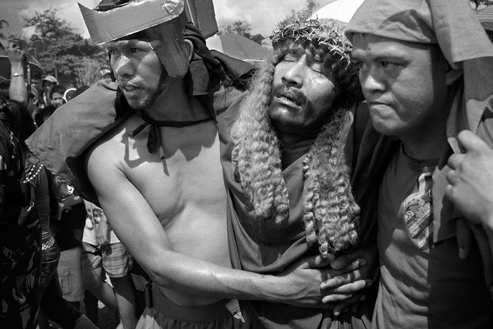 Two men carry an exhausted candidate for crucifixion - a performed the act of Jesus Christ's death.