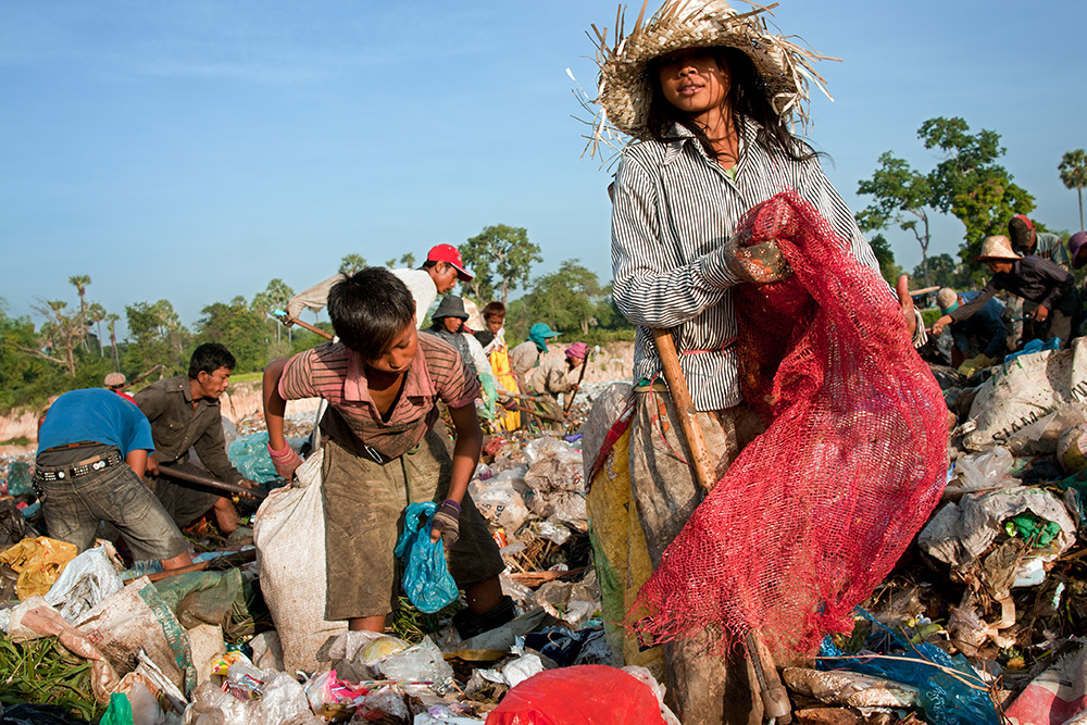 A girl together with other garbage dump residents browse recently dumped waste looking for recyclable material or any other useful objects.