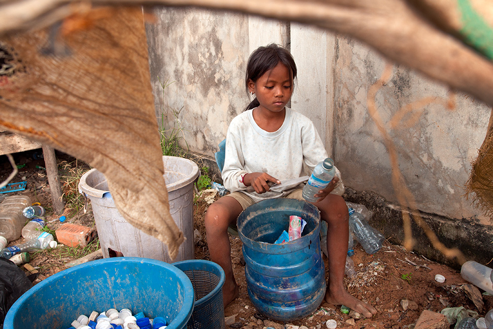 A young girl works in a storage warehouse in Siem Reap. She cleans the bottles with a knife and sort them among the containers.
