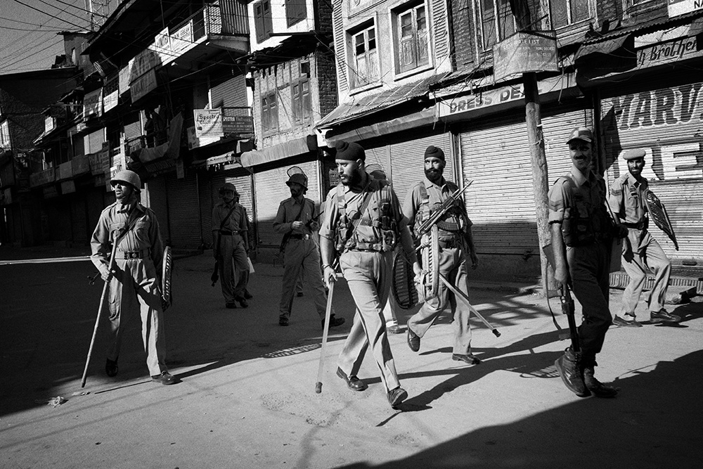 Srinagar. Policemen look from a distance at boys who are throwing stones at them.
