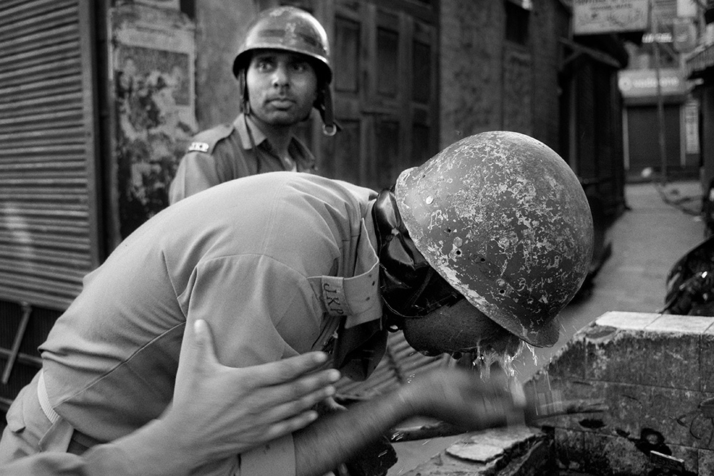 Indian policeman washes his eyes after firing a teargas shell at a stone throwers.